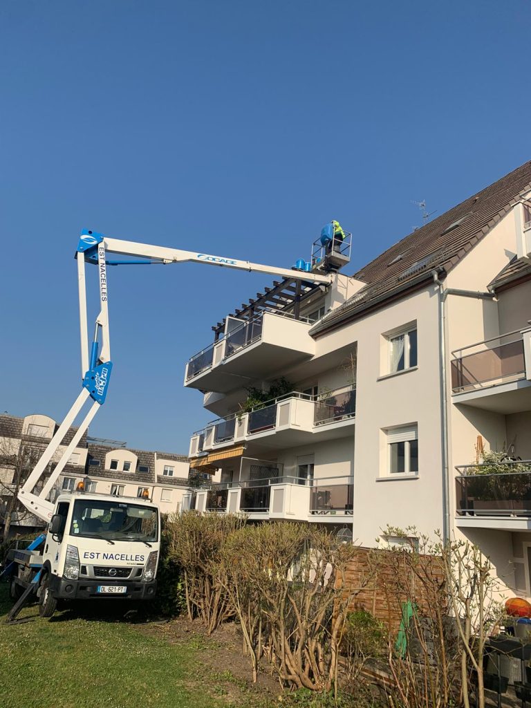 répare toiture - Un ouvrier sur un élévateur à nacelle inspecte ou répare le balcon supérieur d'un immeuble résidentiel à plusieurs étages par temps clair.